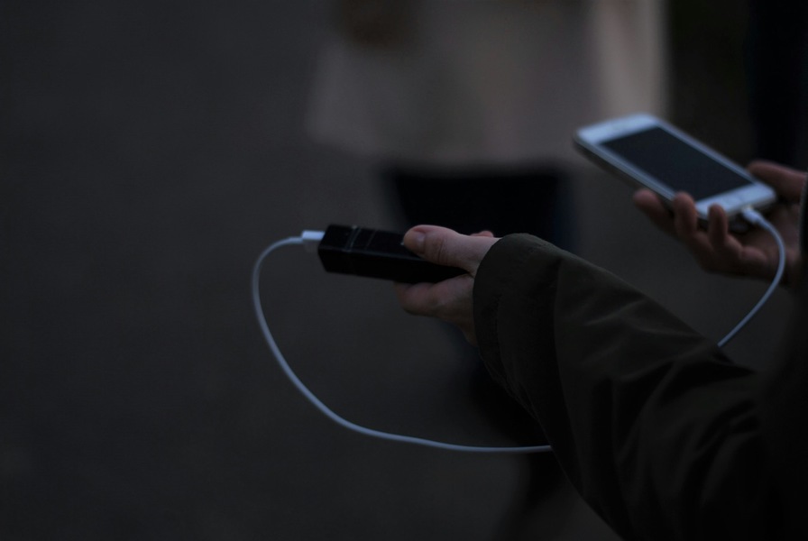 Eine Person hält eine Powerbank in der Hand und lädt damit gerade ihr Mobiltelefon